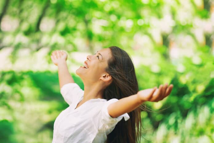 Happy woman breathing fresh clean air outdoor nature forest for spring season pollen allergies. Carefree Asian girl with arms outstretched in freedom. Happiness outside.