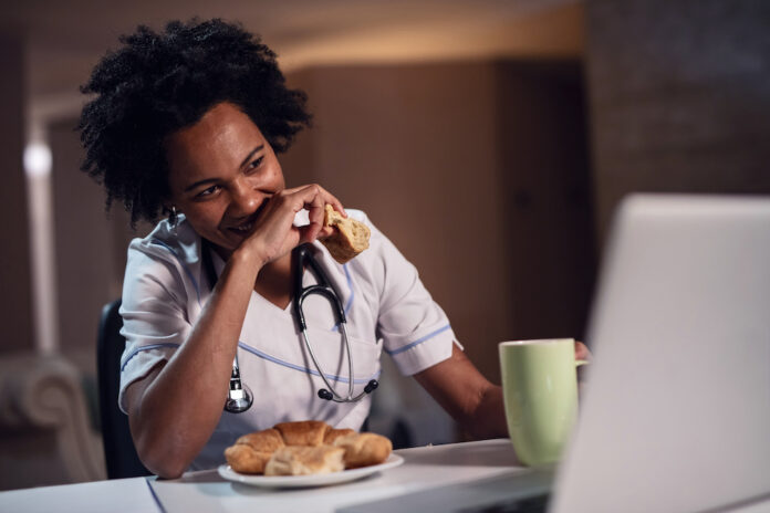 Happy African American doctor enjoying in breakfast time and surfing the internet on computer.